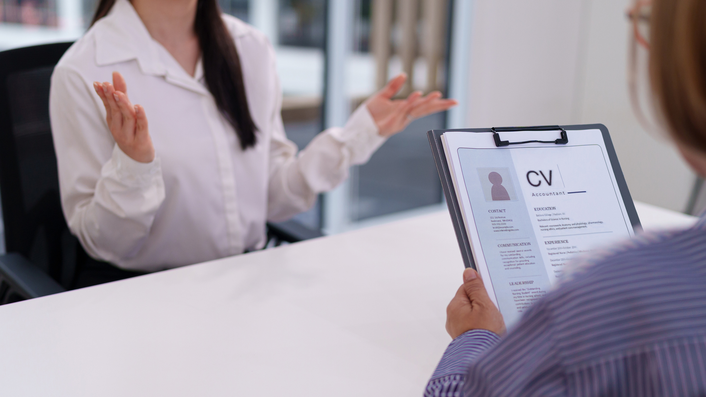 A young Asian woman being interviewed by adult person, reading the resume or CV, ready for the next step in the employment process. Check qualification.